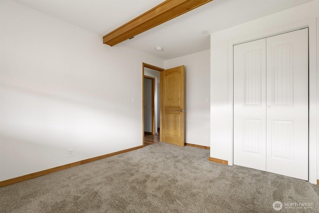 unfurnished bedroom with carpet floors, beam ceiling, a closet, and baseboards