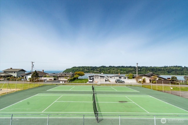 view of tennis court featuring a water view and fence