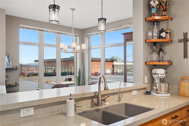 kitchen featuring hanging light fixtures, sink, light stone counters, and a notable chandelier