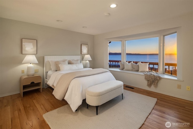 bedroom with multiple windows, light hardwood / wood-style floors, and a water view