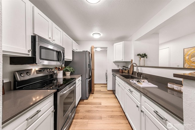 kitchen with sink, white cabinets, light hardwood / wood-style floors, stainless steel appliances, and a textured ceiling