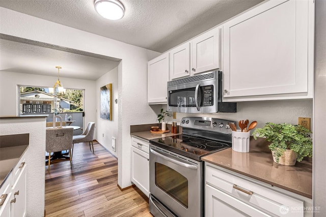 kitchen featuring white cabinets, hanging light fixtures, stainless steel appliances, a textured ceiling, and light hardwood / wood-style flooring