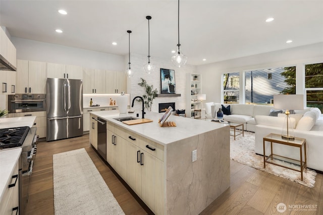 kitchen featuring a center island with sink, appliances with stainless steel finishes, dark wood-type flooring, open floor plan, and a sink