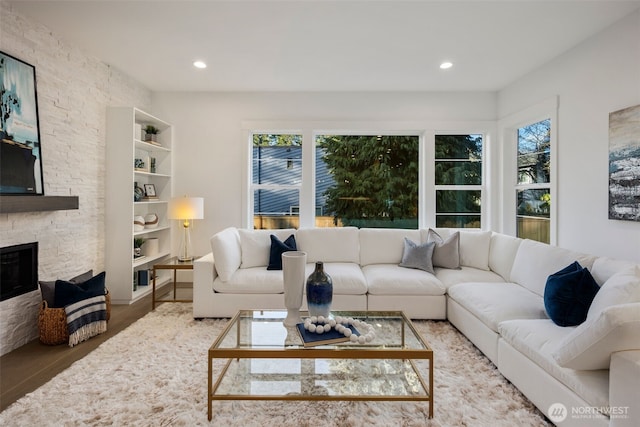 living room featuring recessed lighting, a stone fireplace, and wood finished floors