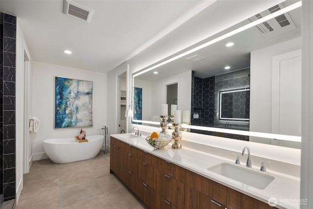 bathroom with tile patterned flooring, a freestanding tub, visible vents, and a sink