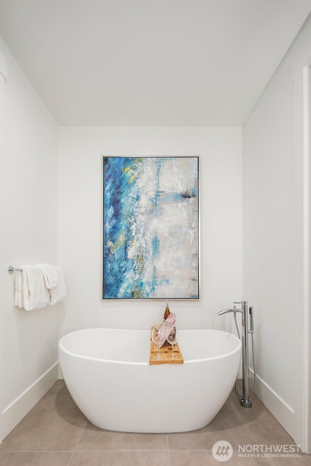 bathroom featuring tile patterned flooring, a freestanding tub, and baseboards