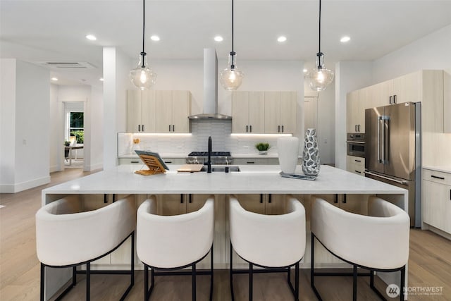 kitchen featuring a breakfast bar area, light wood-style flooring, appliances with stainless steel finishes, modern cabinets, and wall chimney exhaust hood