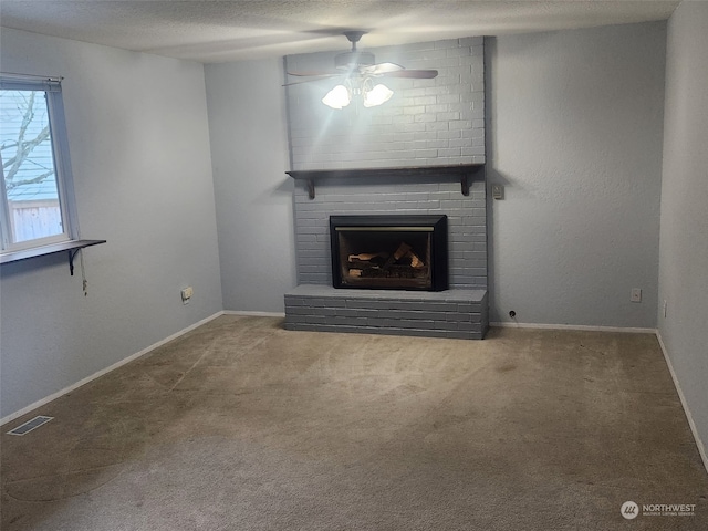 unfurnished living room featuring ceiling fan, a brick fireplace, carpet, and a textured ceiling