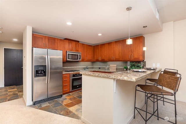 kitchen with a kitchen bar, appliances with stainless steel finishes, kitchen peninsula, pendant lighting, and backsplash