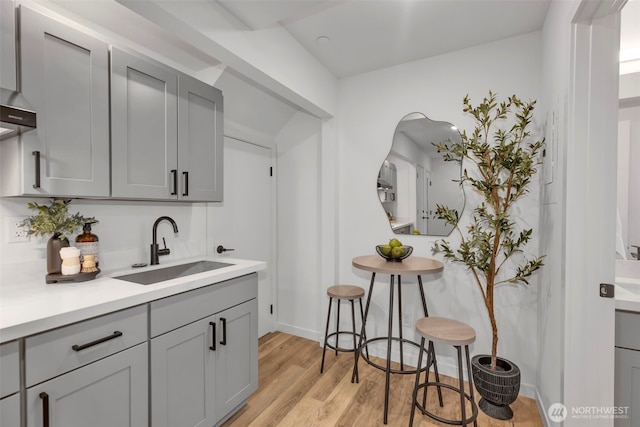 bar with sink, gray cabinetry, light wood-type flooring, and wall chimney exhaust hood