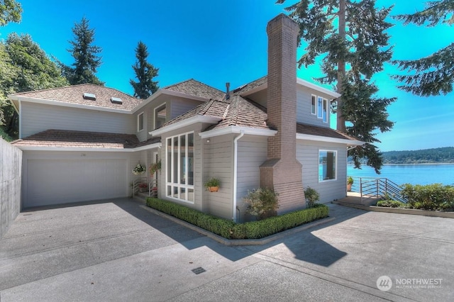 view of front facade featuring an attached garage, concrete driveway, a chimney, and a water view