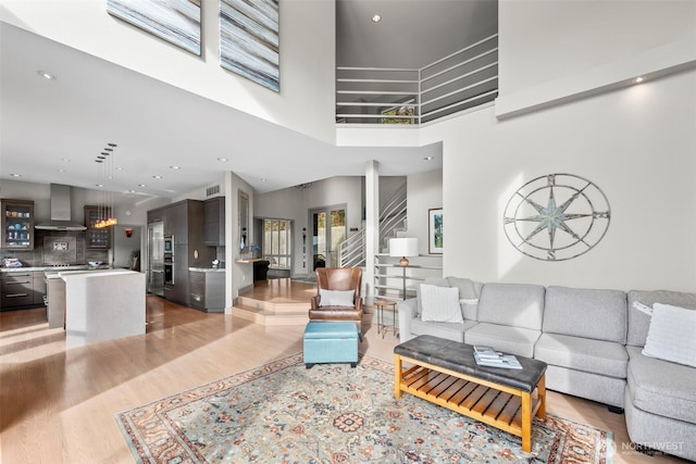 living area featuring light wood finished floors, visible vents, a towering ceiling, stairs, and recessed lighting