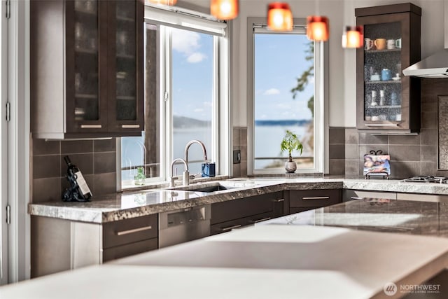 kitchen featuring stainless steel appliances, wall chimney exhaust hood, a sink, and glass insert cabinets