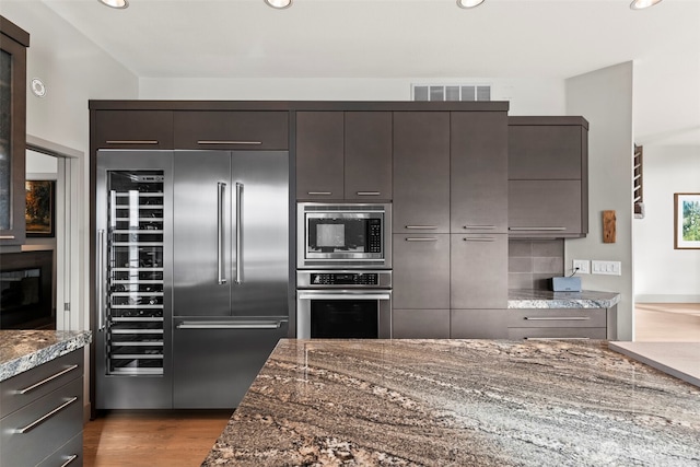 kitchen with visible vents, dark stone countertops, modern cabinets, light wood-type flooring, and built in appliances