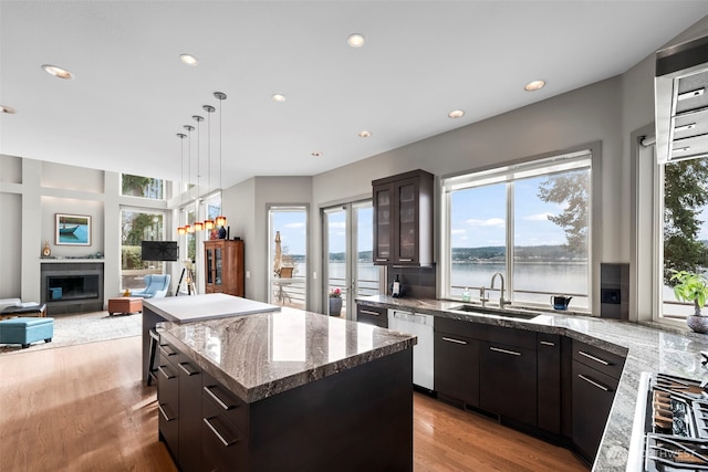 kitchen featuring a water view, a sink, dark brown cabinets, a center island, and glass insert cabinets