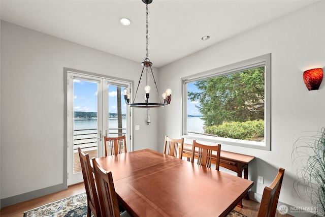 dining room featuring a chandelier, a water view, baseboards, and wood finished floors