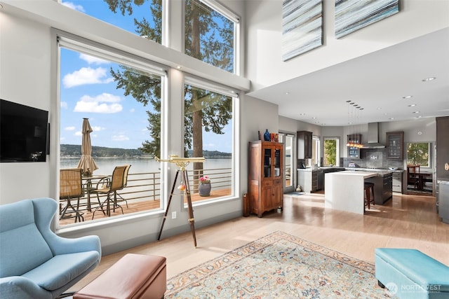 interior space featuring light wood-style floors, recessed lighting, a water view, and a towering ceiling