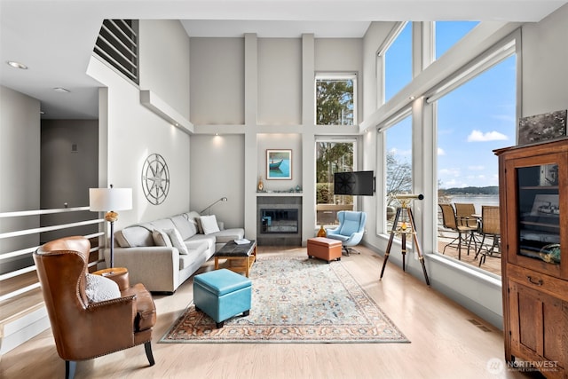 living area with light wood finished floors, a high ceiling, a glass covered fireplace, and a wealth of natural light