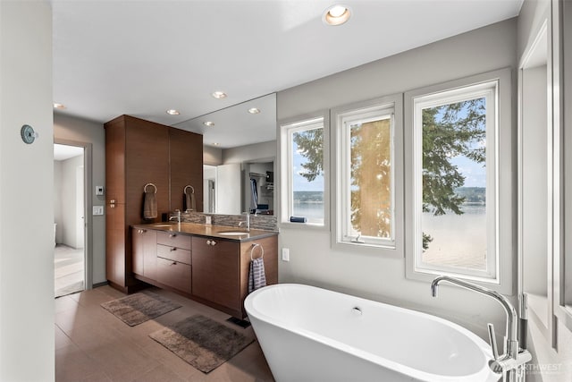 bathroom featuring a sink, double vanity, a freestanding tub, and recessed lighting