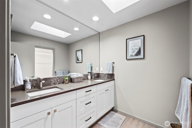 full bathroom featuring double vanity, a skylight, a sink, and wood finished floors