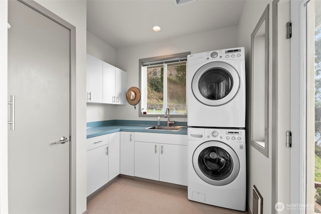 laundry area featuring stacked washer / dryer, a sink, and cabinet space