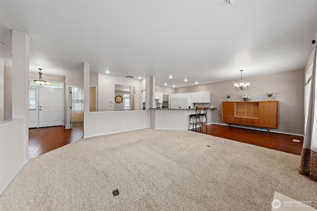 unfurnished living room featuring plenty of natural light, wood finished floors, an inviting chandelier, and carpet floors