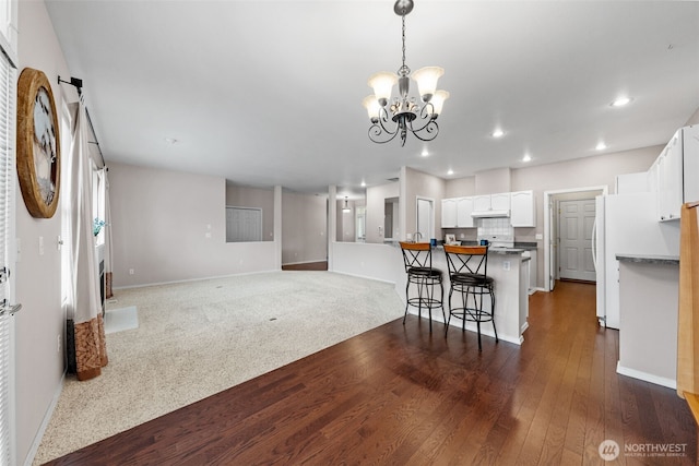 kitchen featuring a kitchen bar, under cabinet range hood, white cabinetry, recessed lighting, and a chandelier