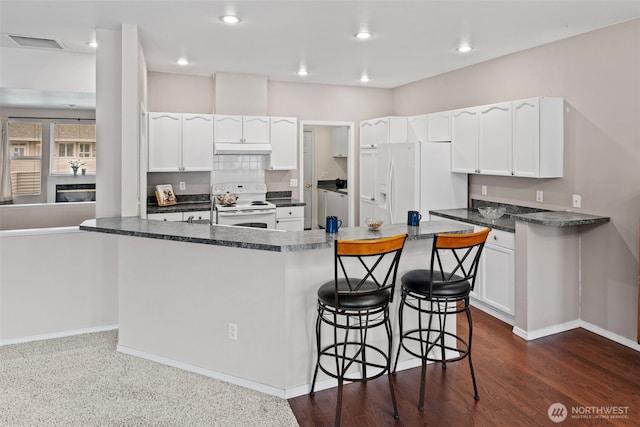 kitchen featuring visible vents, a kitchen bar, under cabinet range hood, white appliances, and white cabinets