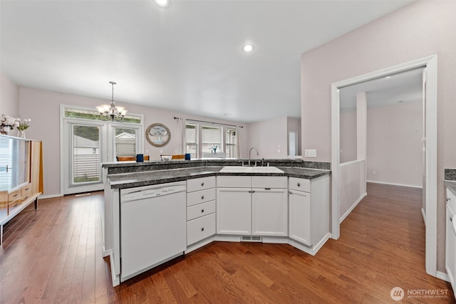 kitchen with wood finished floors, a peninsula, a sink, dishwasher, and a notable chandelier