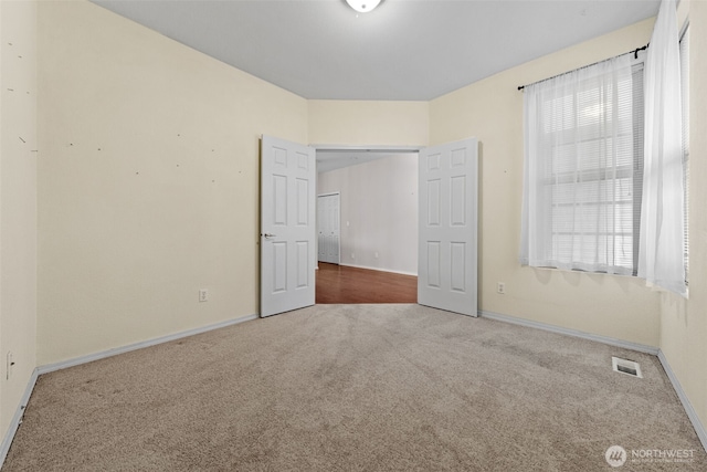 carpeted spare room featuring baseboards, visible vents, and a wealth of natural light