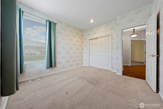 unfurnished bedroom featuring visible vents, a closet, carpet floors, wallpapered walls, and baseboards