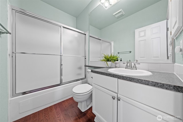 bathroom with vanity, wood finished floors, visible vents, enclosed tub / shower combo, and toilet