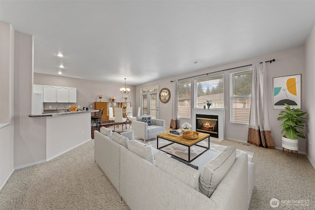 living room with a glass covered fireplace, plenty of natural light, a chandelier, and light carpet