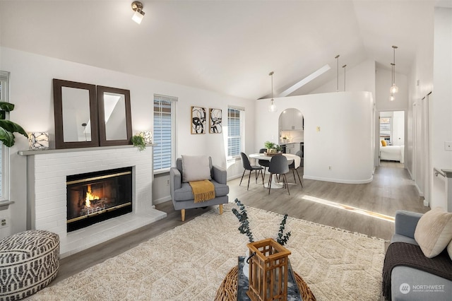 living room featuring a brick fireplace, baseboards, high vaulted ceiling, and wood finished floors