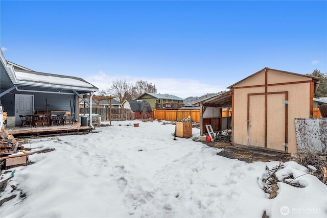 yard covered in snow with an outbuilding, a fenced backyard, a deck, and a shed