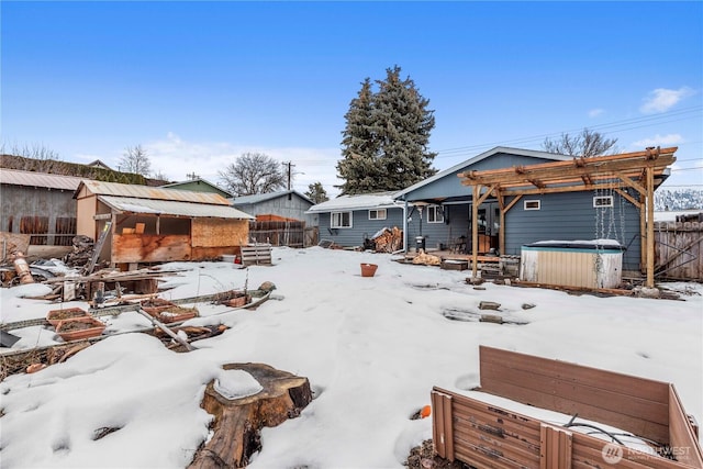 snow covered rear of property featuring fence, a hot tub, an outdoor structure, and a pergola