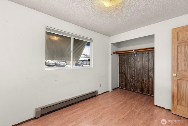 unfurnished bedroom with a closet, a textured ceiling, baseboard heating, and wood finished floors