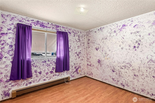 empty room with a baseboard radiator, wood finished floors, a textured ceiling, and wallpapered walls