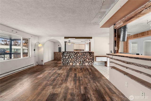 interior space with arched walkways, ceiling fan, wood finished floors, baseboard heating, and a textured ceiling