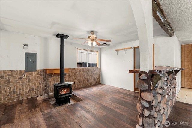 interior space featuring a ceiling fan, a wood stove, electric panel, and wood finished floors