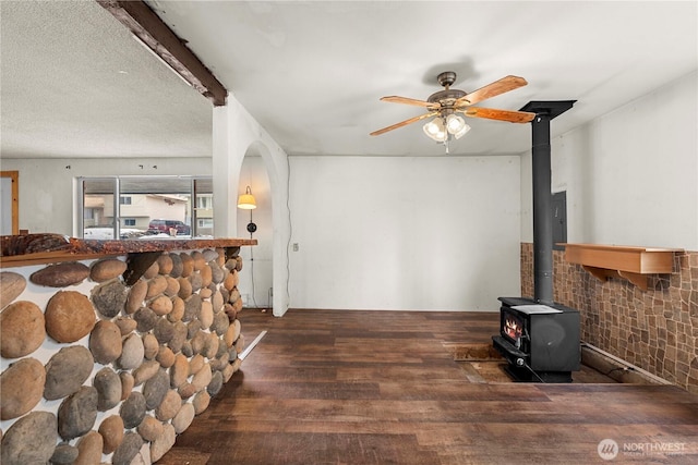 living area with a ceiling fan, a wood stove, and wood finished floors