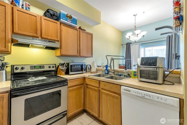 kitchen with appliances with stainless steel finishes, light countertops, under cabinet range hood, a sink, and light tile patterned flooring