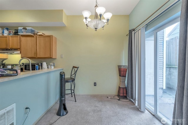 kitchen featuring light colored carpet, visible vents, light countertops, hanging light fixtures, and under cabinet range hood