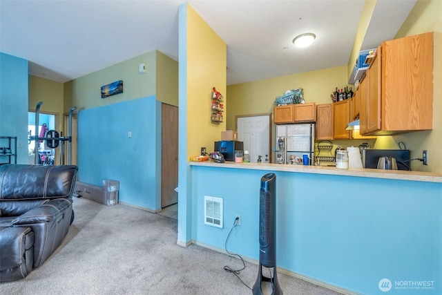 kitchen featuring brown cabinets, light countertops, freestanding refrigerator, light carpet, and under cabinet range hood