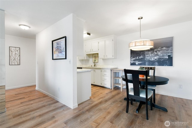 kitchen with white cabinetry, sink, light wood-type flooring, and pendant lighting