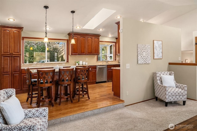 kitchen with a breakfast bar, decorative light fixtures, a skylight, dishwasher, and light carpet