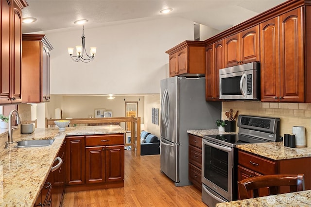 kitchen featuring sink, hanging light fixtures, stainless steel appliances, light stone counters, and light wood-type flooring