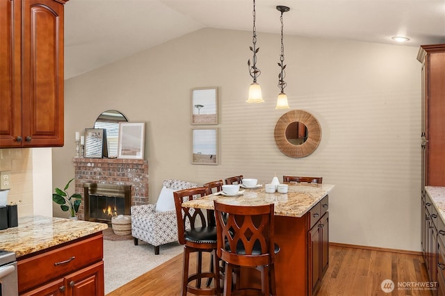 kitchen featuring lofted ceiling, light hardwood / wood-style flooring, a kitchen breakfast bar, pendant lighting, and light stone countertops