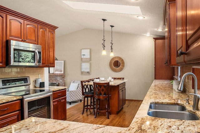 kitchen featuring pendant lighting, sink, lofted ceiling, appliances with stainless steel finishes, and light wood-type flooring