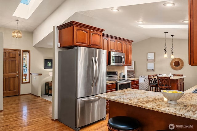 kitchen with decorative light fixtures, light wood-type flooring, appliances with stainless steel finishes, vaulted ceiling with skylight, and light stone countertops